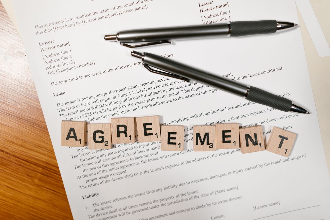 services-01 A document with Scrabble tiles spelling 'AGREEMENT' and two pens, symbolizing contract signing.