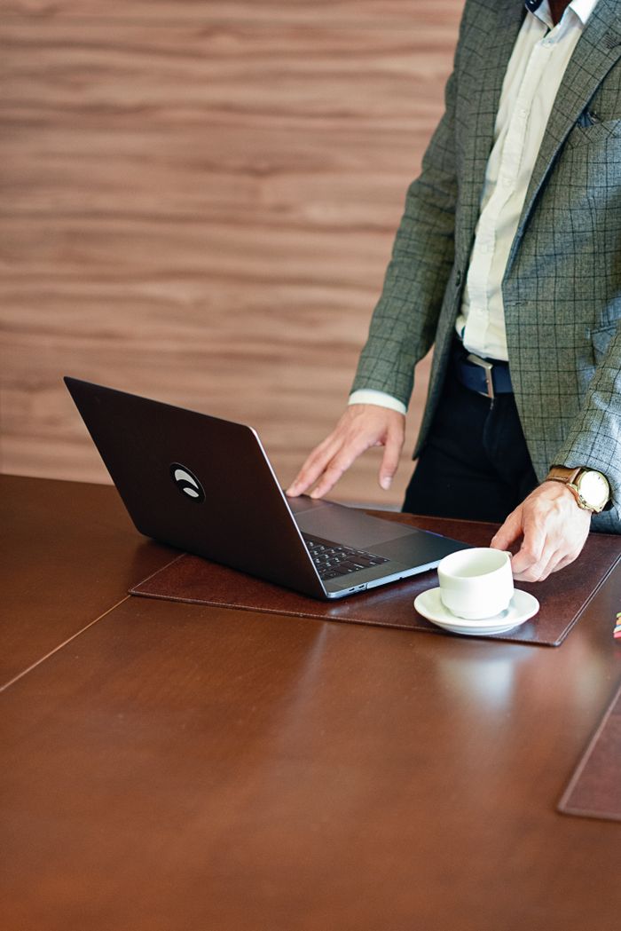 Business professional in a suit using a laptop on a wooden desk with a cup of coffee.